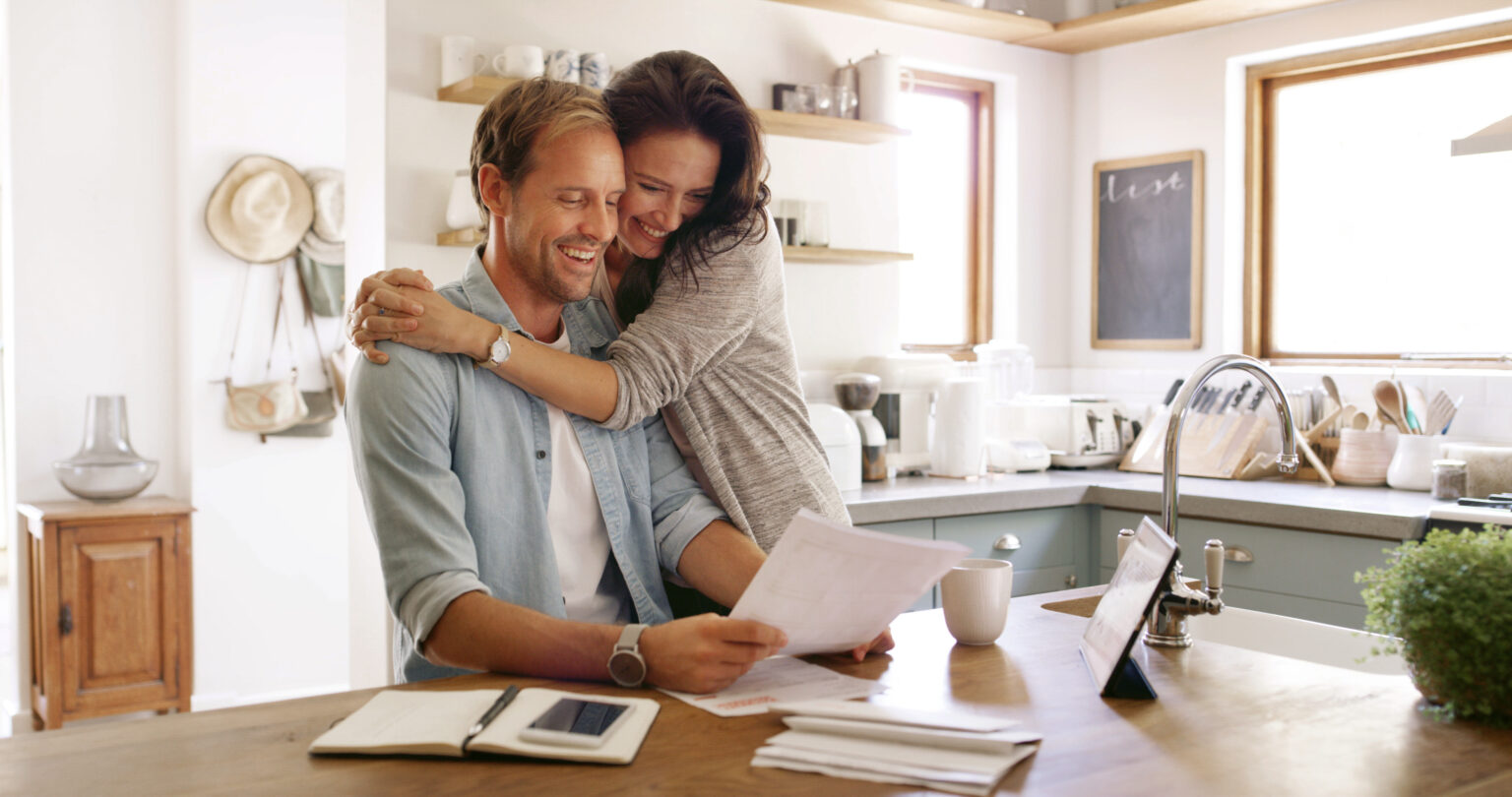 Home, hug and couple with documents, smile and payment for mortgage, rent and love. Apartment, finance and man with woman in kitchen, embrace and paperwork report for savings and investment growth.