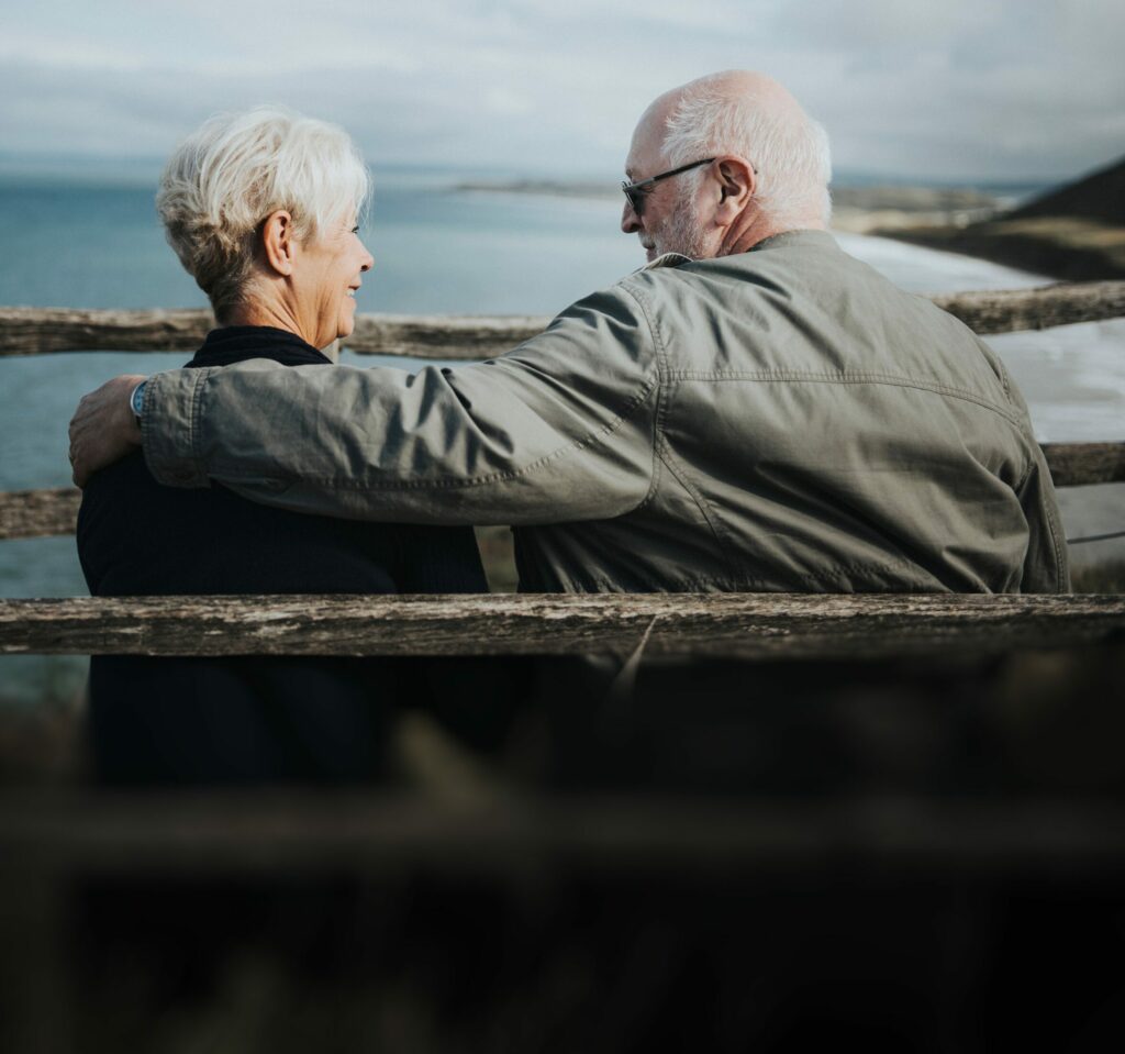 Older couple sat on bench looking happy and together